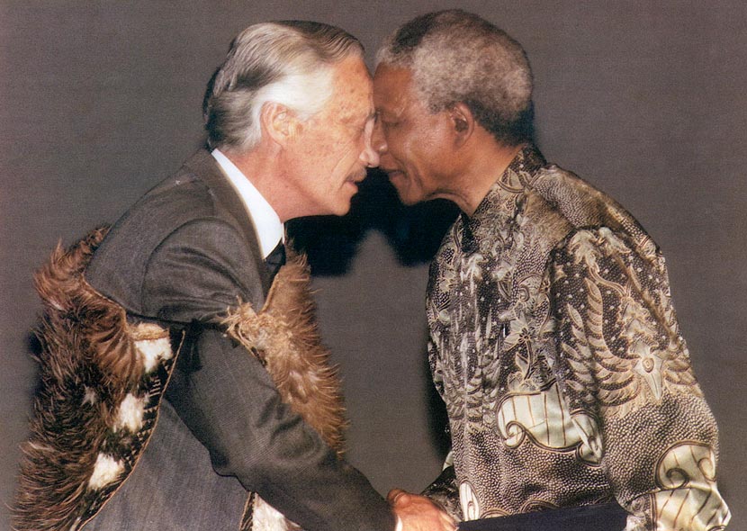 A profile photograph showing Mandela and Kawharu engaged in a hōngi (pressing noses together in greeting). Kawharu wears a kahukiwi (Māori cloak of kiwi feathers).