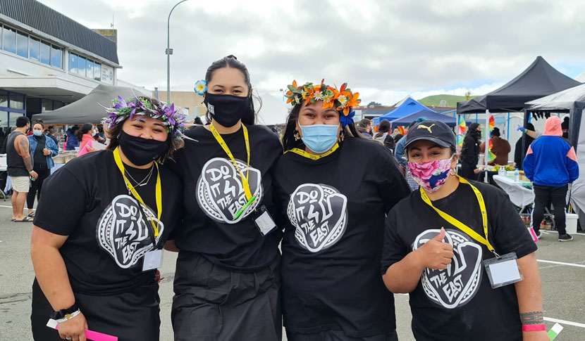 Four women wearing masks at an outdoor event with stalls in the background.