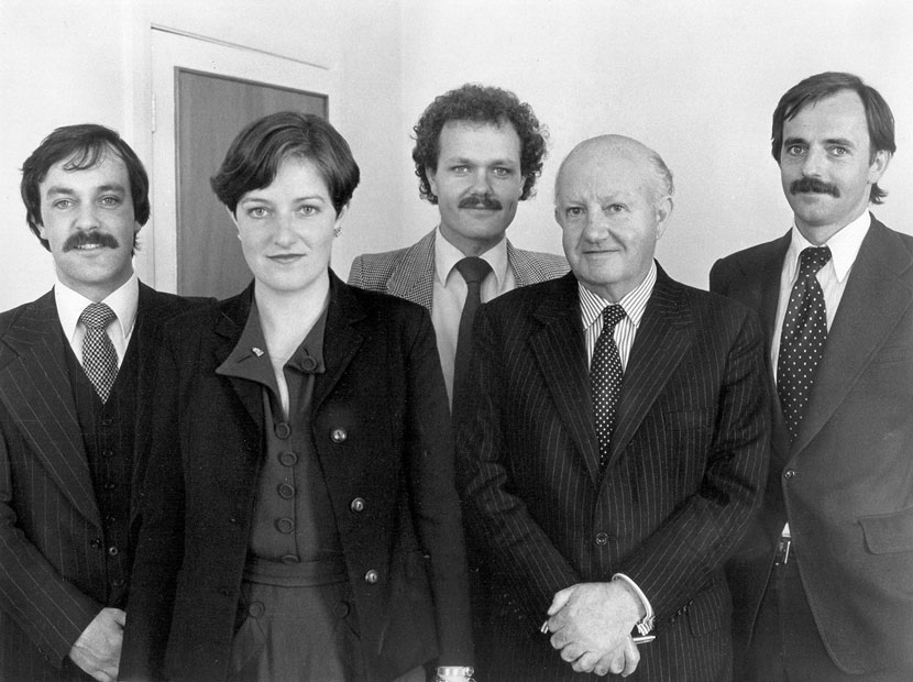 Four men and one woman standing in a line, formally dressed.