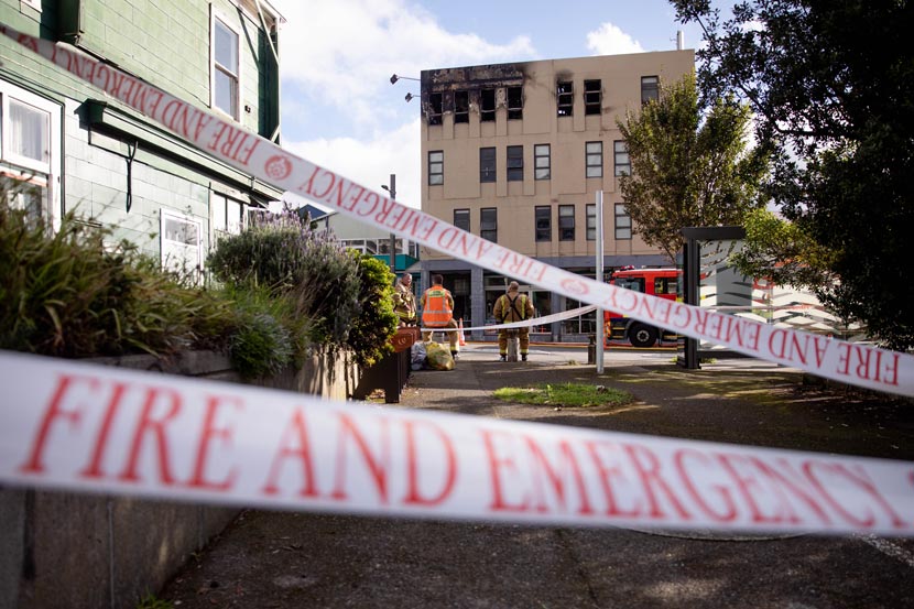 White tape with the words Fire and Emergency in front of fire blackened building on city street