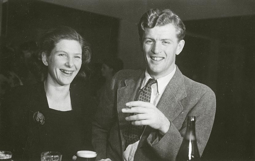 A young man and woman smiling at the camera, a bottle of beer in front of them. 
