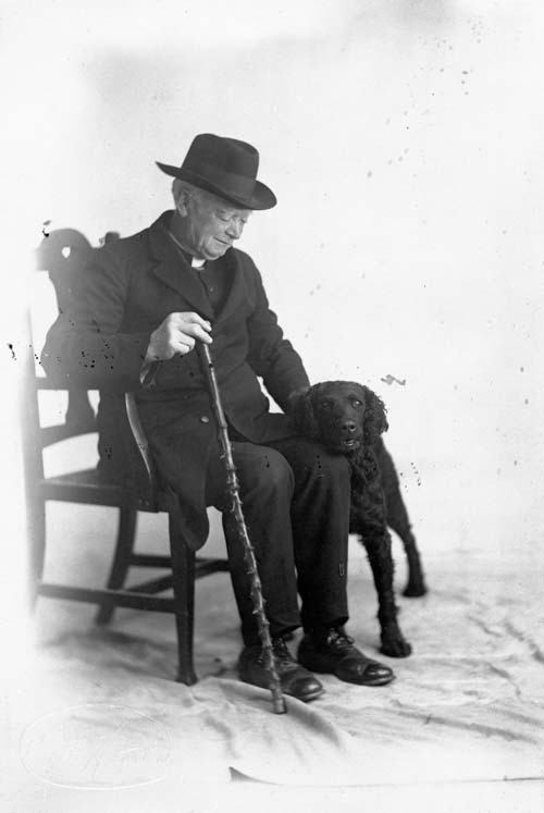 Elderly man seated with a walking cane, and a dog nestling against his leg