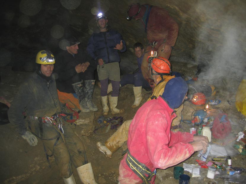A large group of people, wearing helmets and overalls, clustered in a muddy cave.