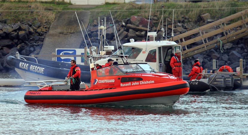 An orange Coastguard boat with a blue boat labelled NZAS rescue anchored near land.