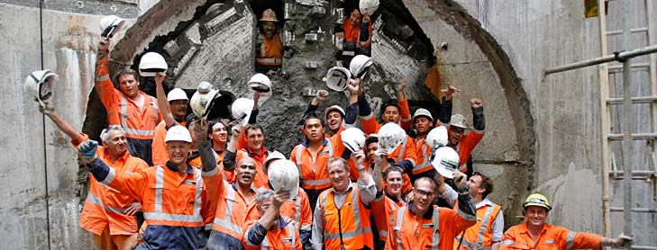 Workers in hi-vis vests and safety helmets celebrating in front of tunnel