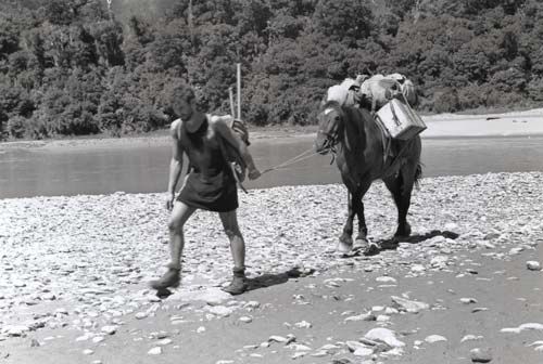 Man walking a horse laden with bags over a stony river bed