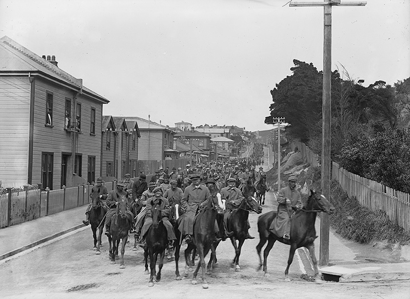 Large group of men on horseback riding down suburban street
