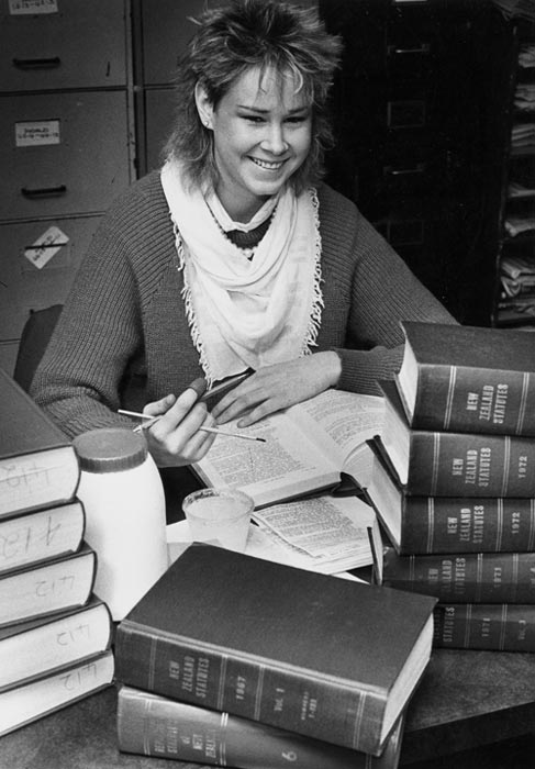 Woman pasting paper in book on desk full of statute books