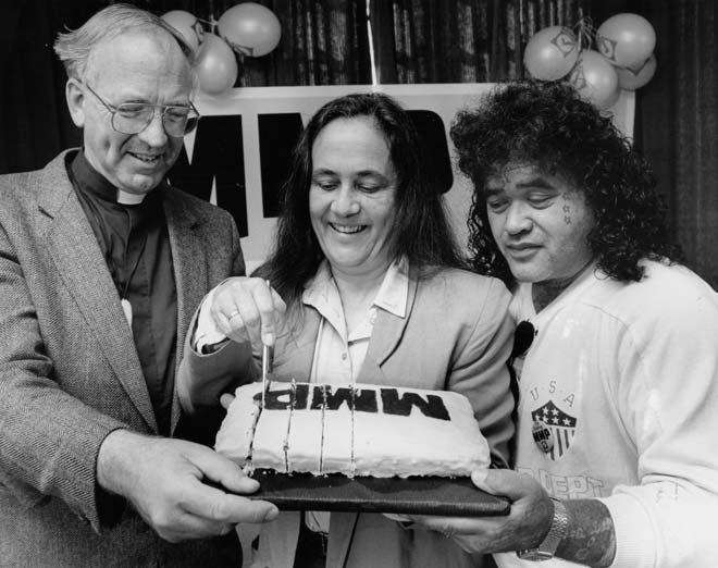 Three people around MMP cake with lit candle