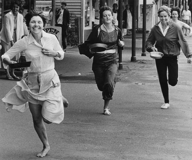 Three women running down street holding frying pans