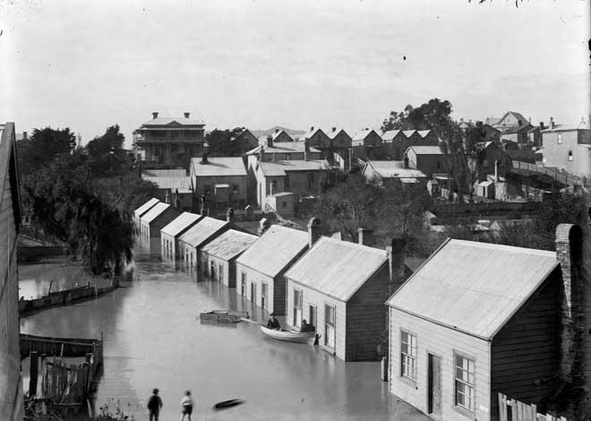 A row of eight flooded cottages, and people in a rowboat.