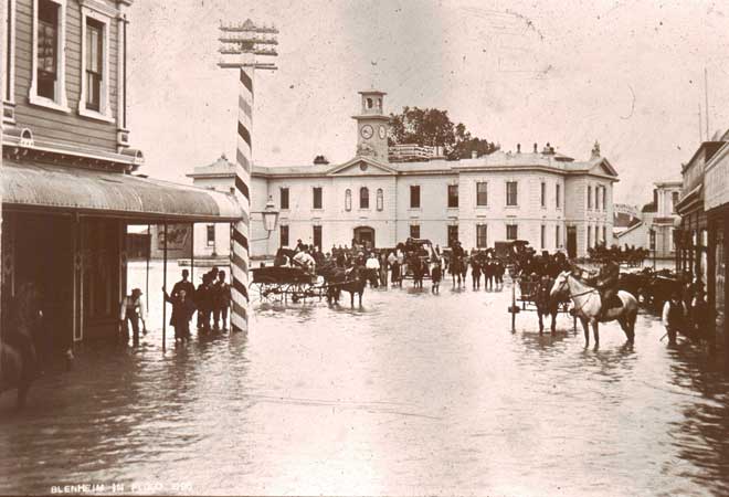 A flooded city street with a crowd of people and horses.