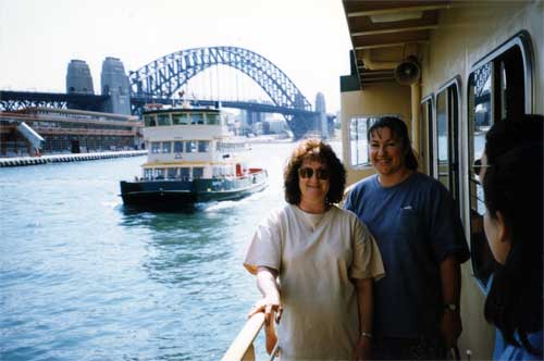Two women standing on ship walkway on harbour with arch bridge in background
