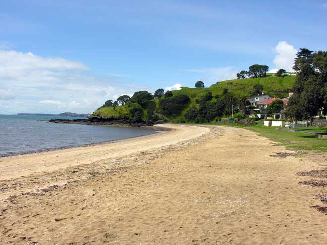 Beach with green hills and a few houses in background