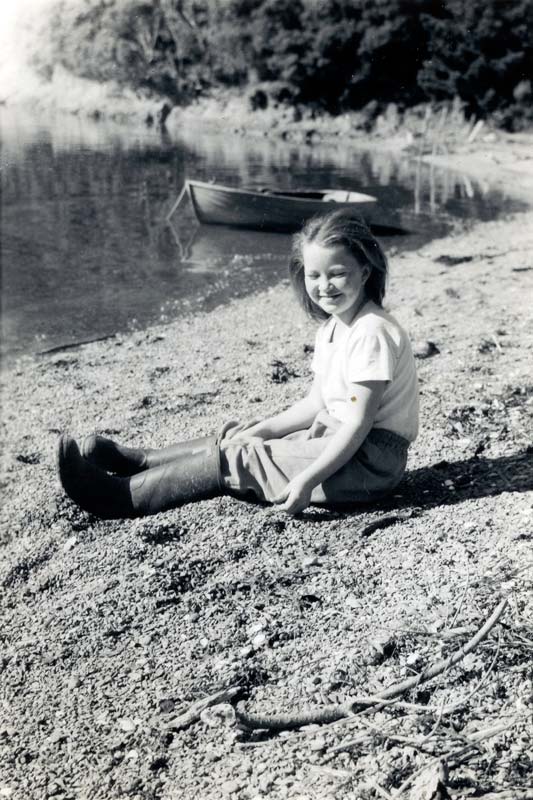 Girl sitting on a beach with dingy moored in background