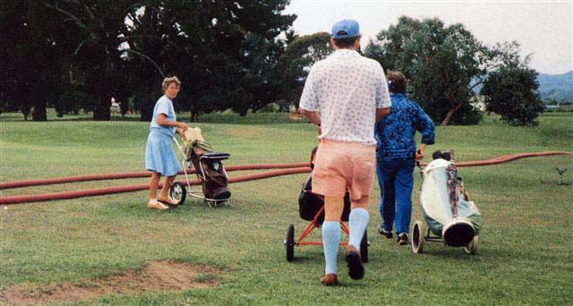 Golf players on a golf course covered with red fire hoses.