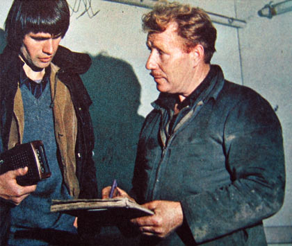 Two men in work clothes discussing information in book