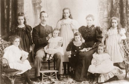 Family group of nine with baby sitting on father's kneww