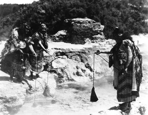 Three Māori women cooking food in flax kits in a hot pool