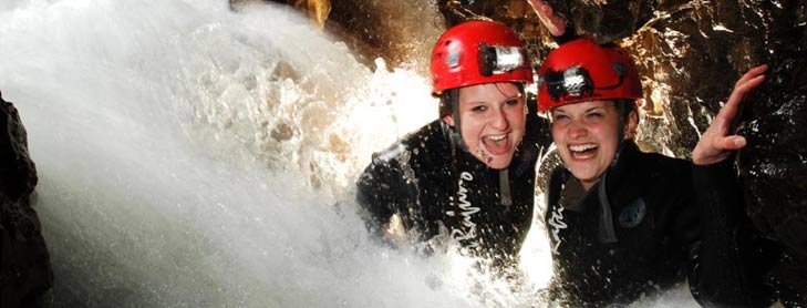 Two people in red safety helmets laughing as water rushes over them in cave