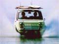 Car with surfboards on the roof drives through shallow water at speed