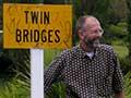Man standing next to sign that says 'Twin Bridges'