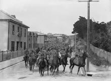 Large group of men on horseback riding down suburban street