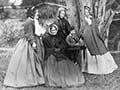 A photograph of a group of women and a boy under a tree, some seated and some standing
