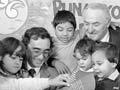 Young children read a picture book with two men.