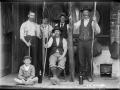 Group of men on porch holding up two enormous eels. A boy sits in front